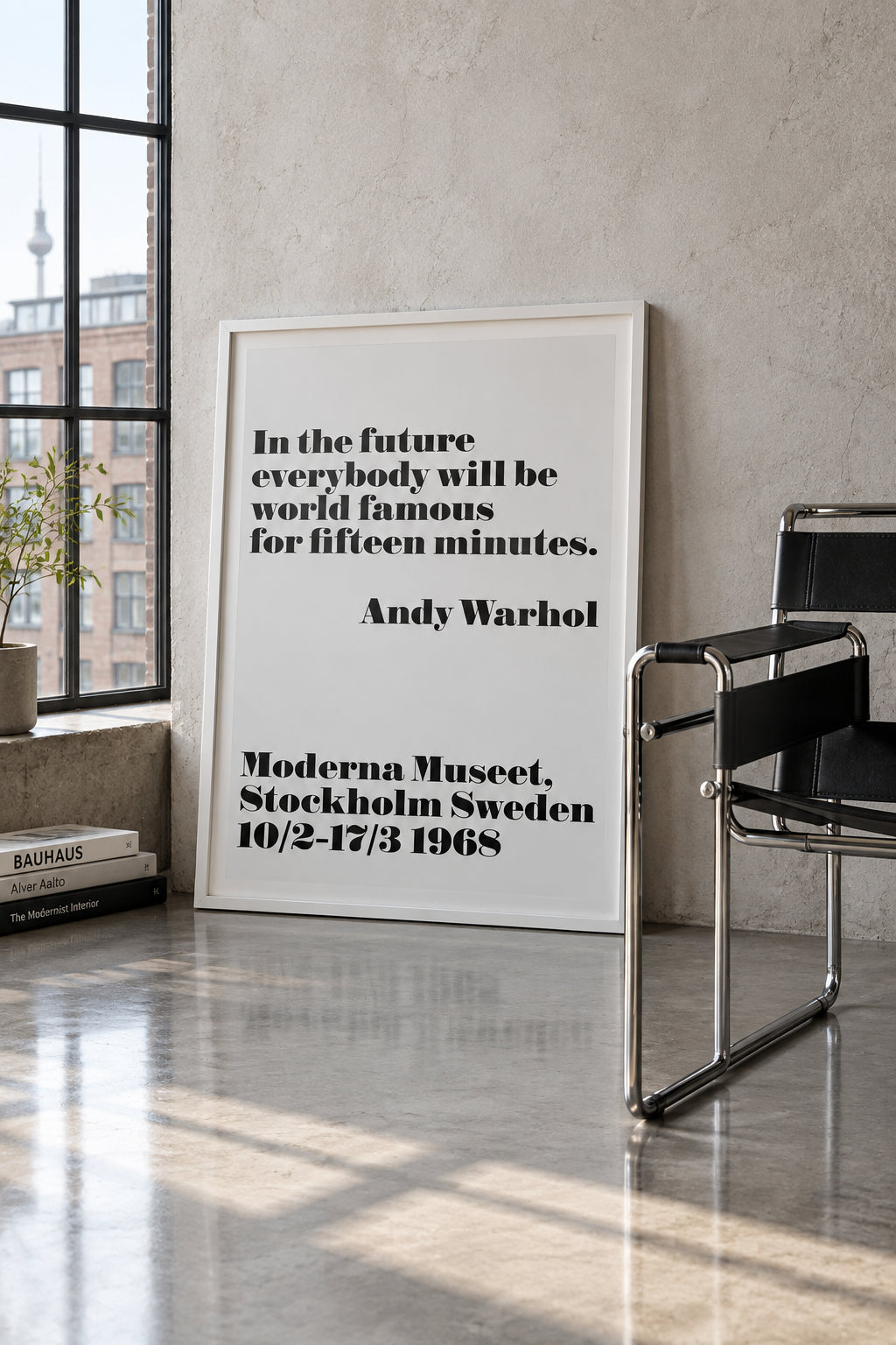Andy Warhol "In the future everybody will be world famous for fifteen minutes" poster, shown framed, leaning against a concrete wall beside a tubular steel chair.