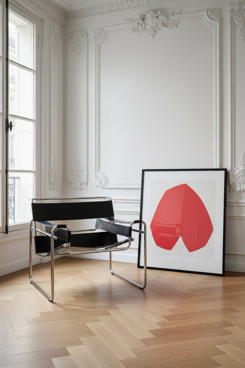 Ellsworth Kelly, Red White (1962) art print, shown framed, leaning against a white panelled wall beside a tubular steel chair.